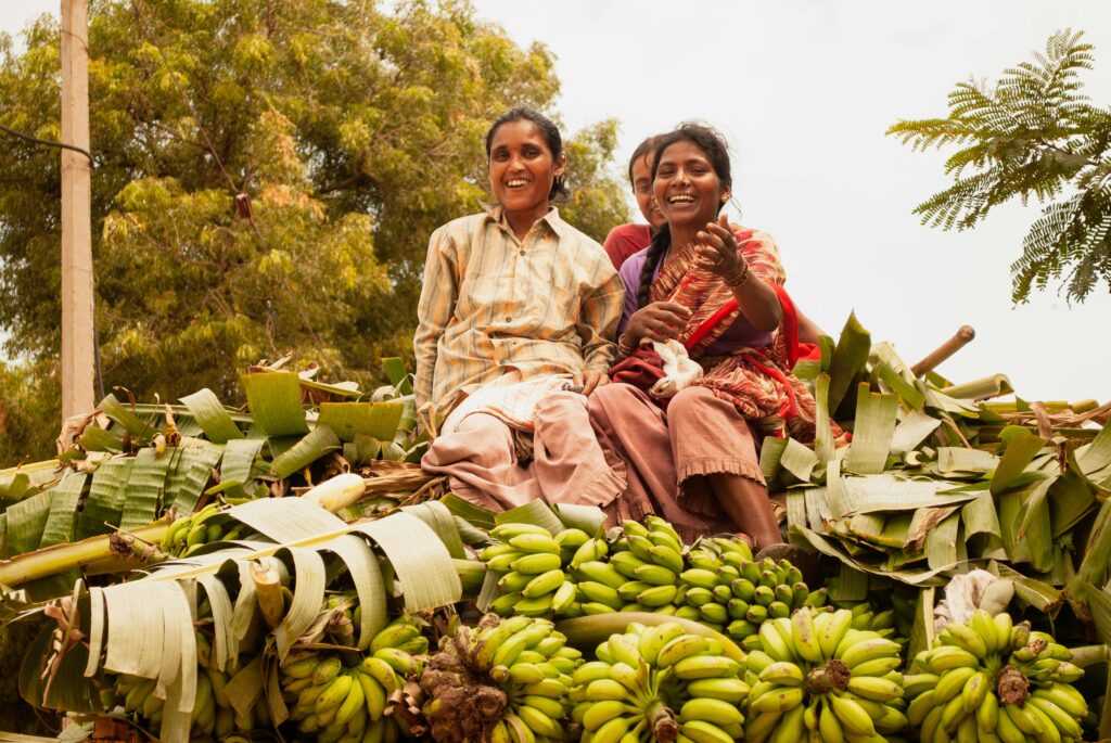 Women on a banana-laden cart smiling after harvest in Hampi, India.